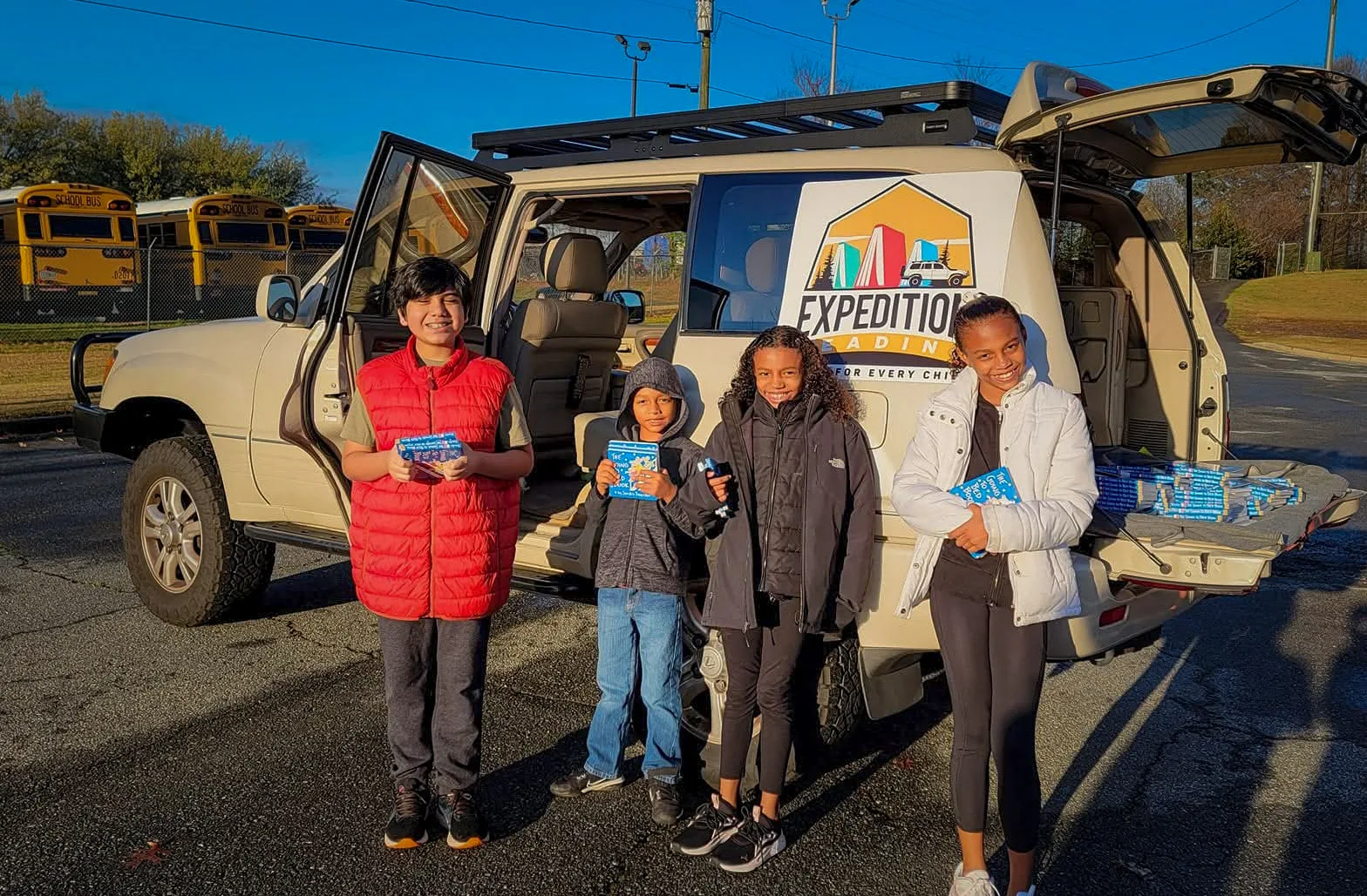 Four children stand beside the Expedition Reading delivery vehicle, each holding a book they just received